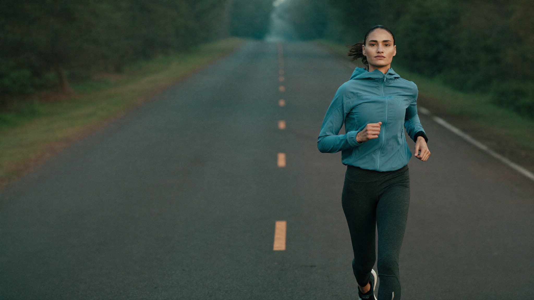 Woman running device-free on an open road — WE-STIM fabric, nothing to carry